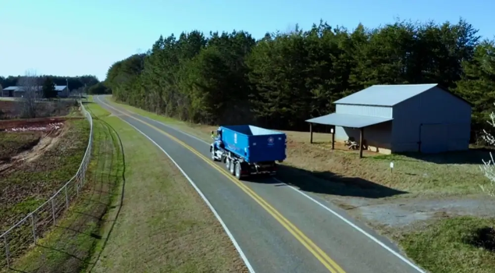 Blue dumpster truck driving on rural road