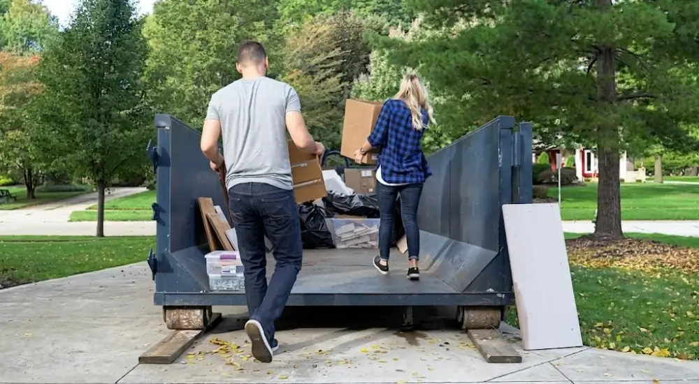 Couple carrying boxes into rental dumpster