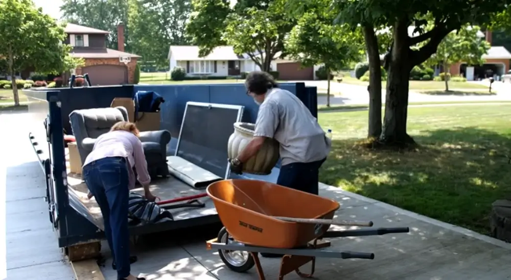 Couple loading furniture and junk into dumpster