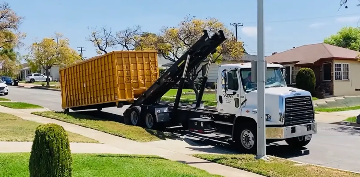 Dumpster delivery truck lifting a yellow roll-off container for drop-off at a Sarasota home